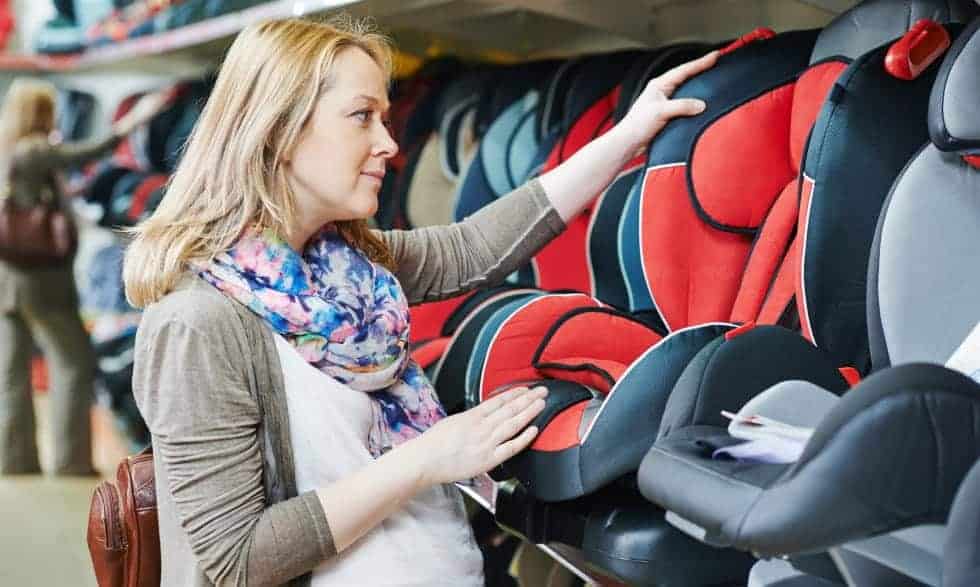 A pregnant woman looks for a suitable child car seat in a shop